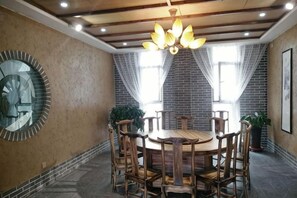 A dining area with a round table and chairs, a large mirror on the wall, and a brick wall with windows. - Shenghua Culture International Hotel (Linze)
