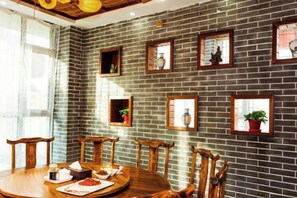A dining area with a brick wall, wooden chairs, a round table, and framed pictures. - Shenghua Culture International Hotel (Linze)