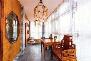 Un comedor con mesa y sillas de madera, una araña y ventanas amplias.