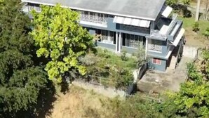 A large, two-story building with a flat roof, surrounded by dense greenery. - Fruitful paradise 
Charming house with WiFi 
welcoming you to enjoy and relax (Church Corner)