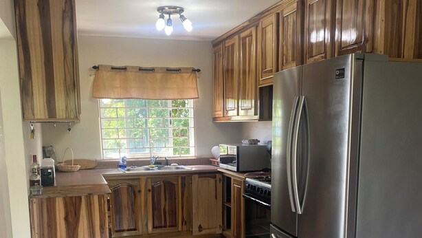 A kitchen with wooden cabinets, a stainless steel refrigerator, a sink, and a window with a view of greenery. - Fruitful paradise 
Charming house with WiFi 
welcoming you to enjoy and relax (Church Corner)