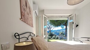 Ein Schlafzimmer mit Bett, Nachttischlampe, einem Blumentopf und Blick ins Freie.