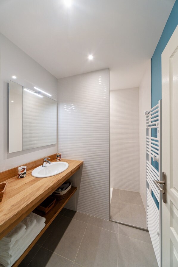 A modern bathroom with a wooden vanity, two sinks, a large mirror, and a walk-in shower.