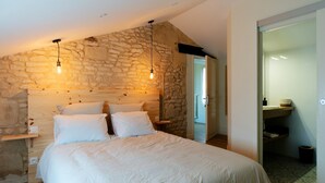 A bedroom with a stone wall, a wooden headboard, a bed with white bedding, and two hanging light fixtures.