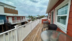 A wooden deck with a glass table and chairs, white railings, and a view of neighboring buildings. - Parrot Cottage - Margaritaville District (Fort Myers Beach)