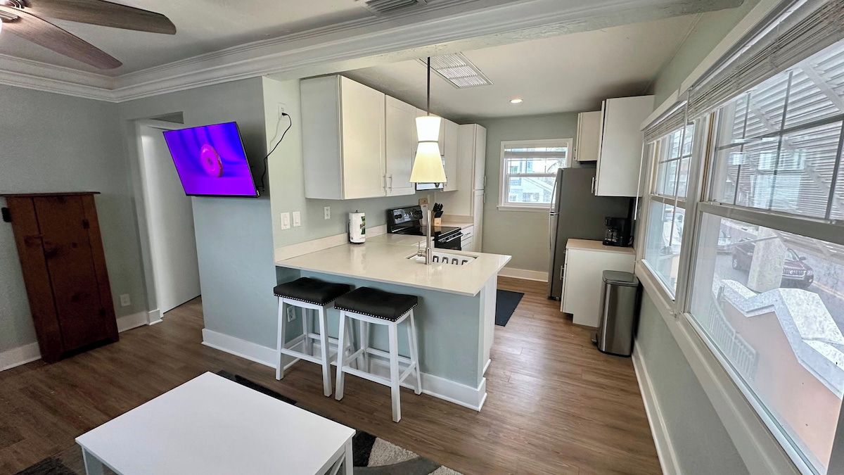 Une cuisine moderne avec un coin bar, des meubles blancs et un téléviseur à écran plat fixé au mur.