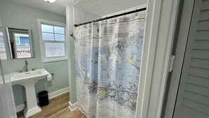 A bathroom with a sink, mirror, and a shower curtain with a map design. - Parrot Cottage - Margaritaville District (Fort Myers Beach)