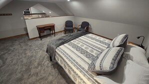 Une chambre à coucher comprenant un lit, deux chaises, un bureau et un plafond en pente doté d’un éclairage encastré.