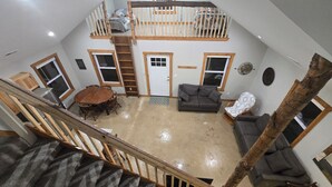 Un loft spacieux avec un plafond haut, un escalier en bois, un coin repas et un salon comprenant un canapé et un fauteuil.