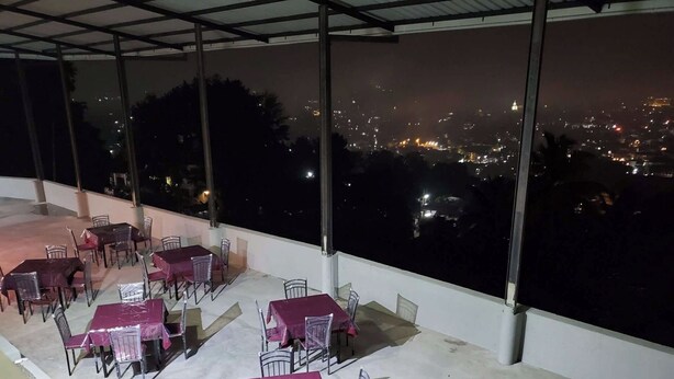 An outdoor dining area with tables and chairs, covered by a roof, overlooking a cityscape at night. - Serene Kandy Getaway with City Views (Kandy)