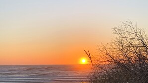 A beach scene with the sun setting over the ocean, surrounded by sand and sparse vegetation. - 3BD/2BA, Walkable, Family/Dog Friendly, Deck, BBQ, WIFI in Quaint Rockaway Beach (Rockaway Beach)