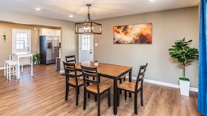 A spacious dining area with a wooden table and chairs, a modern chandelier, and a large abstract painting on the wall.