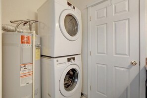 A laundry area with stacked appliances, including a dryer and a washing machine, next to a white door.