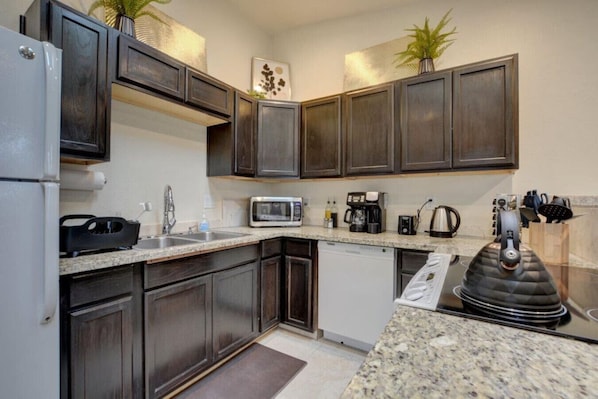 A modern kitchen with dark wood cabinets, granite countertops, a built-in microwave, a coffee maker, and a kettle.