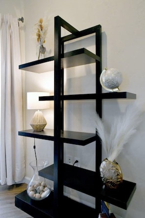 A black shelving unit with decorative items including a globe, a vase with feathers, and a lamp. - Beautiful Loft Apartment w/Views in Medford, OR! (Medford)
