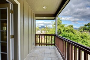 A covered balcony with a tiled floor and a wooden railing, overlooking a green landscape with trees and a distant mountain. - Beautiful Loft Apartment w/Views in Medford, OR! (Medford)