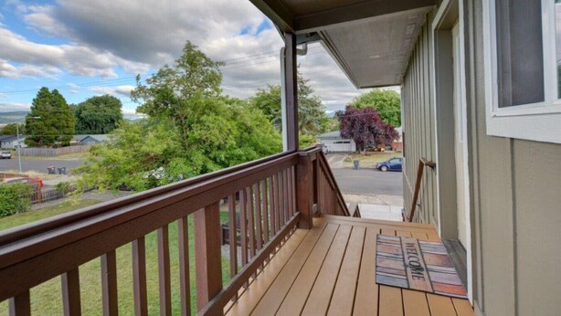 A wooden deck with a wooden railing, a welcome mat, and a view of a residential street with houses and trees. - Beautiful Loft Apartment w/Views in Medford, OR! (Medford)