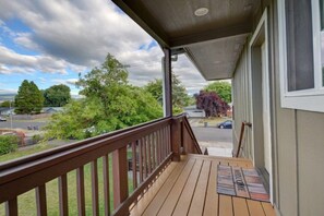 Eine Holzterrasse mit Holzgeländer, einer Fußmatte und Blick auf eine Wohnstraße mit Häusern und Bäumen.