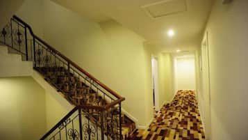 Escada com corrimão de madeira e grades de metal preto, que leva a um quarto com piso xadrez.