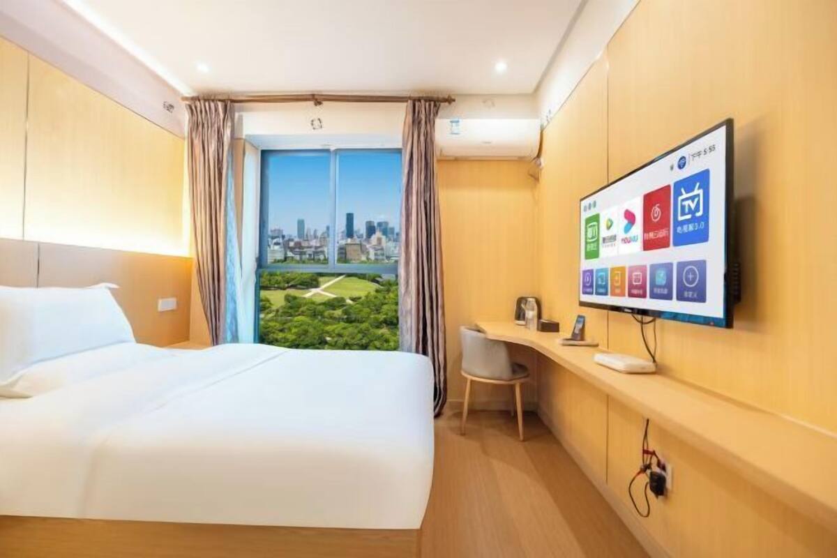 Een hotelkamer met een bed, bureau, televisie en uitzicht op een stadsbeeld.