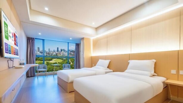 Una habitación de hotel moderna con dos camas, vistas a la ciudad y un pequeño rincón de descanso.