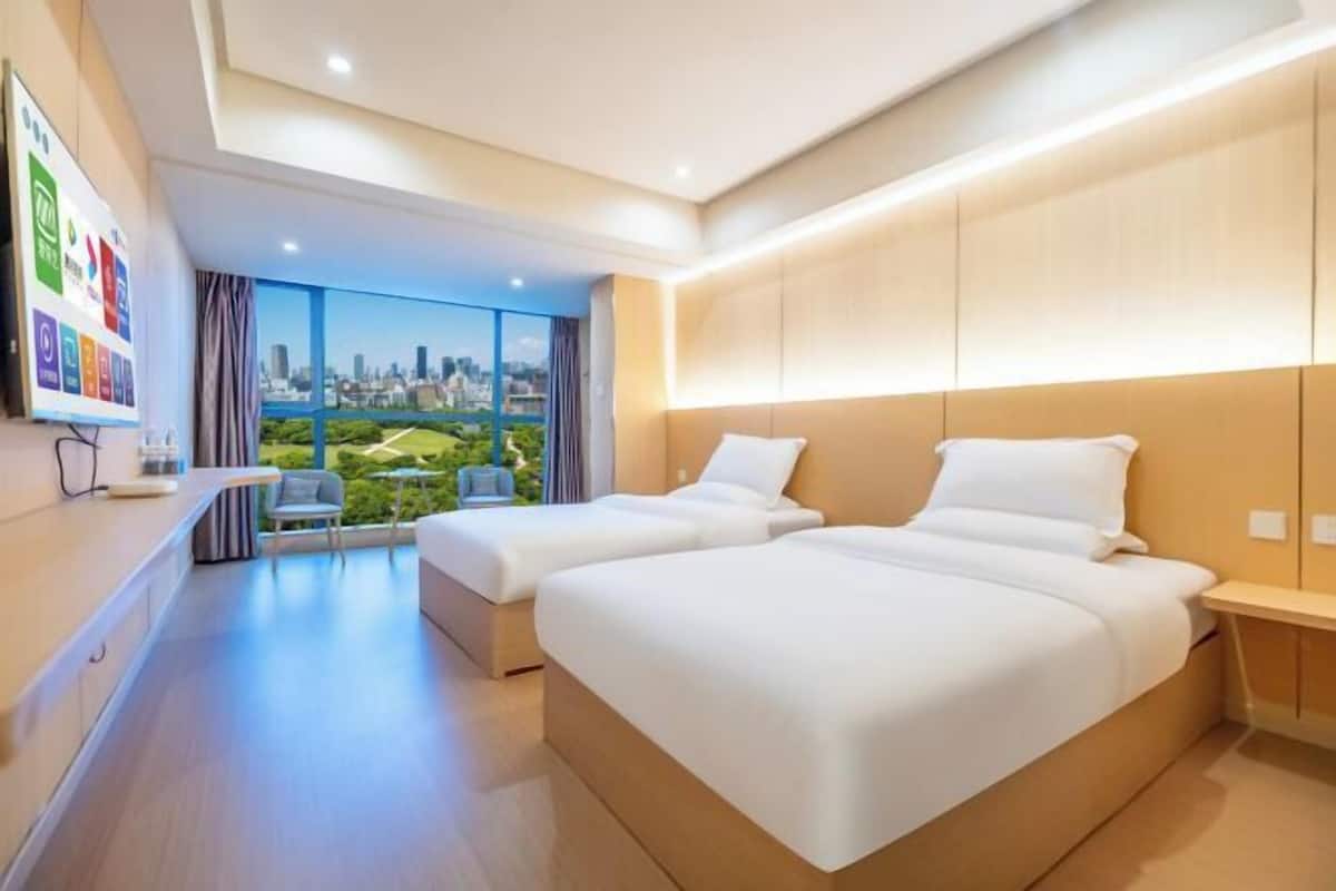 Een moderne hotelkamer met twee bedden, uitzicht op de stad en een klein zitgedeelte.