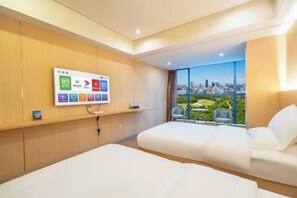 Ein Hotelzimmer mit Blick auf die Stadt, einem an der Wand befestigten Fernseher und zwei Betten.