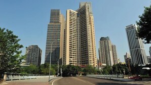 Un paisaje urbano con edificios altos, cielo despejado y una carretera con un puente en primer plano.