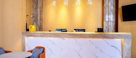 Zona de recepción de un hotel con mostrador de mármol, asientos y un televisor montado en la pared.