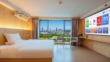 Quarto de hotel com uma cama grande, uma escrivaninha com cadeira, uma televisão exibindo os serviços do hotel e vista para a cidade através de amplas janelas.