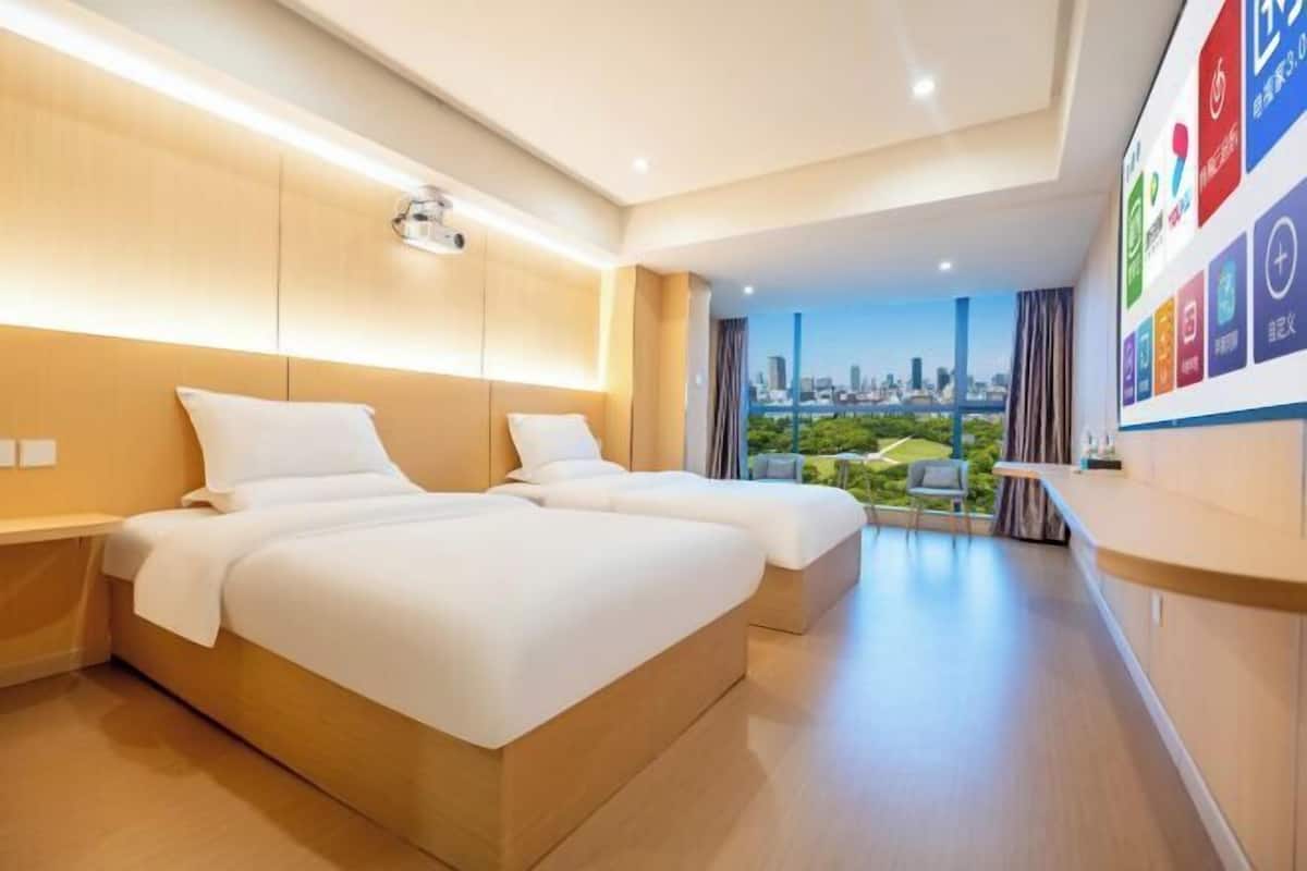 Een hotelkamer met een bed, een bureau, een stoel en uitzicht op de stad.