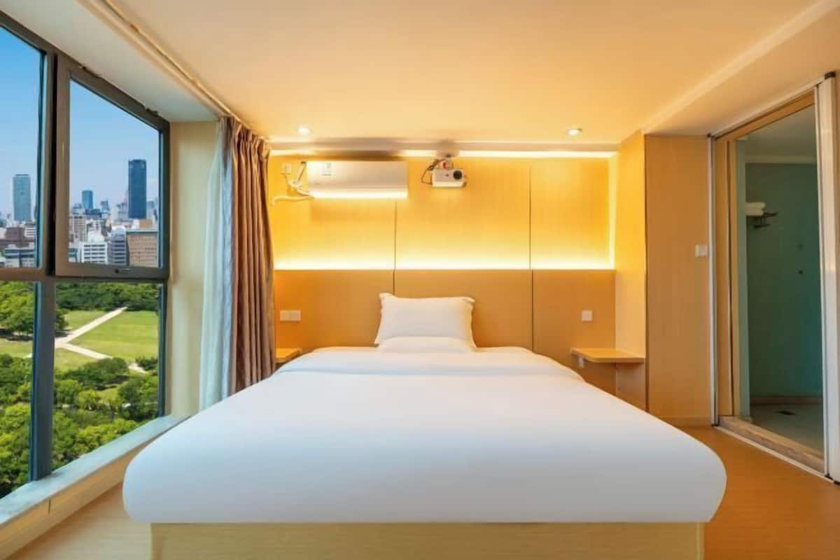 Een moderne hotelkamer met een groot bed, uitzicht op de stad en een schuifdeur naar een balkon.