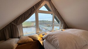 A bedroom with a sloped ceiling, large windows, and a view of a bridge over water.