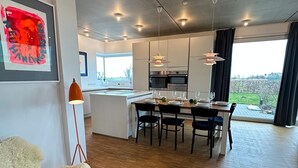 A modern kitchen with a dining area, wooden flooring, and large windows offering a view.