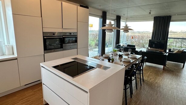 A modern kitchen with white cabinetry, a central island, and a dining area with a view.