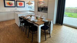 A modern kitchen with a central island, pendant lights, and a dining area with a wooden table set for four.