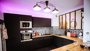 A modern kitchen with dark cabinetry, a stainless steel oven, a tiled backsplash, and a wooden countertop. - L'Échappée Parisienne - Canal St-Denis (Aubervilliers)