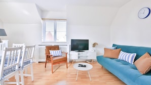 Una sala de estar moderna con un sofá azul, sillas blancas, un televisor y un reloj en la pared.