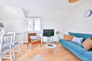 A modern living room with a blue sofa, white chairs, a TV, and a clock on the wall. - 2 Bed House Near Beach with Free Parking (Barry)
