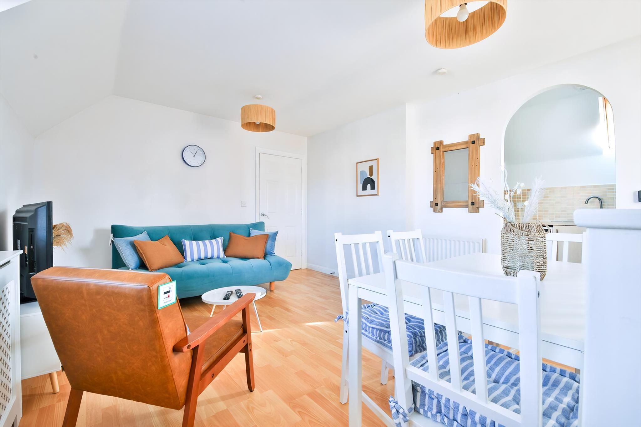 A living room with a blue sofa, a wooden chair, a white dining table, and a crib with blue bedding.