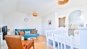 Una sala de estar con un sofá azul, una silla de madera, una mesa de comedor blanca y una cuna con ropa de cama azul.