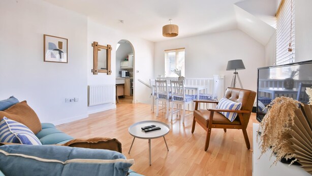 Una sala de estar moderna con un sofá, una mesa de centro, una zona de comedor con sillas, un televisor y una cocina al fondo.