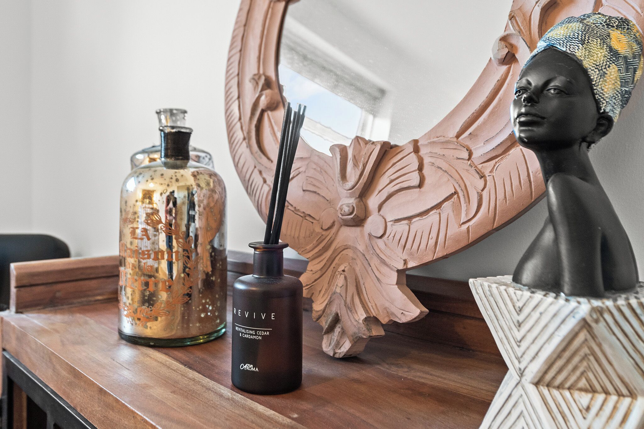 A wooden table with a glass bottle, a dark bottle with a label, and a decorative wooden sculpture.