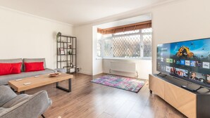 A modern living room with a sofa, coffee table, TV, and bookshelf. - Bright & Spacious 4BR House | Elizabeth Line - Pass the Keys (London)