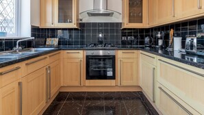 A modern kitchen with wooden cabinets, a black tiled backsplash, a stainless steel range hood, and a black marble floor. - Bright & Spacious 4BR House | Elizabeth Line - Pass the Keys (London)