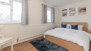 A bedroom with a bed, a radiator, a window with curtains, a chair, and artwork on the wall. - Bright & Spacious 4BR House | Elizabeth Line - Pass the Keys (London)