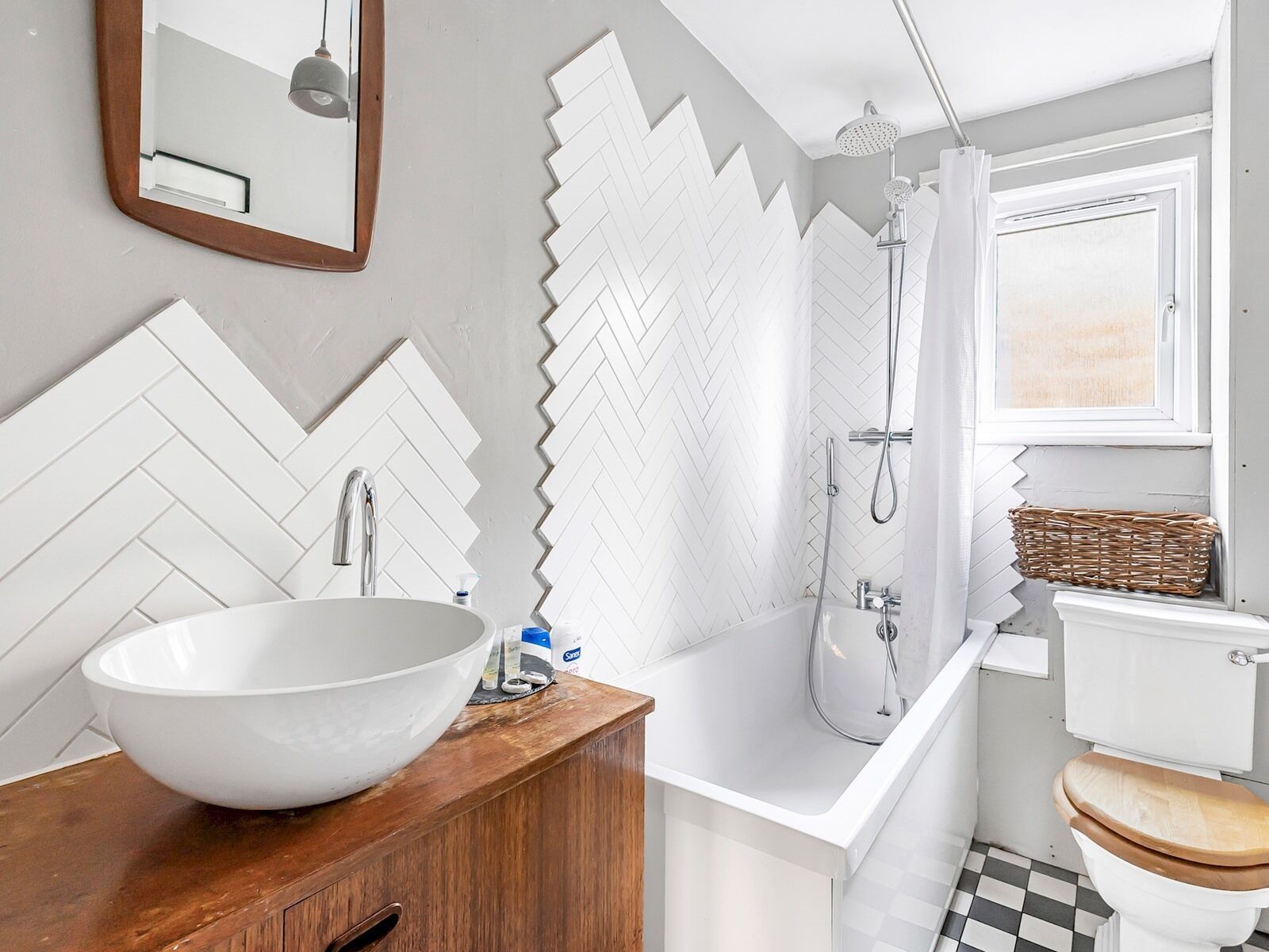 Ein Badezimmer mit einem großen, weißen Waschtisch, einer Holz-Kommode, einer weißen Toilette mit Holzsitz, einer Dusche mit weißer Duschvorhang und einer Wand mit Zickzackmuster.