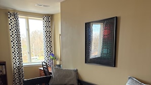 A bedroom with a large bed, a desk, a chair, a bookshelf, and a window with patterned curtains.