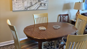 A dining area with a round wooden table, six chairs, a chandelier, and a large black and white cityscape painting on the wall.