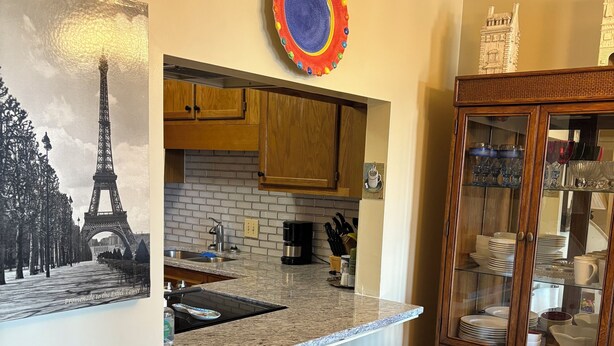 A kitchen with a white bar counter, wooden cabinets, a coffee maker, and a decorative plate on the wall.
